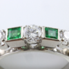 Meine Damen und Herren, erfreuen Sie Ihre Augen an einem exquisiten Stück, das heute zur Versteigerung steht – ein prächtiger Ring aus 585er Weißgold, ein wahres Wunderwerk der Handwerkskunst! Mitten in dieser schillernden Schönheit befindet sich ein zentraler Diamant im Brillantschliff, der mit unvergleichlicher Brillanz strahlt und glänzt. Auf beiden Seiten flankieren ihn nicht nur ein, sondern zwei atemberaubende Smaragde im Carréschliff – sehen Sie sich diesen leuchtenden Grünton an! Und gerade wenn Sie denken, es kann nicht besser werden, sorgen wir mit zwei kleineren Diamanten im Brillantschliff, die jede Seite schmücken, für etwas Glanz. Alle Steine sind selbstbewusst auf einem polierten Metallband gefasst, das so glatt ist, dass es wie die Morgensonne auf einem schlichten weißen Hintergrund glänzt. Wer wird das Gebot für dieses wunderbare Meisterwerk abgeben? Verpassen Sie es nicht – sichern Sie sich diesen Schatz noch heute!