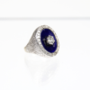 Der 750/Weißgold-Ring ist auf einem schlichten weißen Hintergrund zu sehen und besticht durch ein strukturiertes Band mit einer auffälligen, runden Fassung aus blauem Emaille. In der Mitte befindet sich ein ca. 0,5 Karat schwerer VVS/G-Diamant, der elegant von 26 kleineren G/VS-Diamanten mit insgesamt ca. 0,39 Karat umgeben ist.