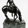 Eine bronzene, patinierte Skulptur von Albert Hinrich Hussmann mit dem Titel „Frauenakt mit Draperie auf Pferd“, die eine Person zeigt, die seitlich auf einem Pferd sitzt, das zu grasen scheint. Das Stück ist signiert und auf einem Sockel aus grünem Marmor montiert.