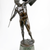 Die Statue mit dem Titel „Ludwig Eisenberger – Krieger mit Speer“ zeigt einen bronzenen patinierten Krieger, der einen Speer und einen Schild umklammert. Die Figur ist auf einem Sockel aus grünem Marmor montiert und hat eine dynamische Haltung, die Bewegung oder Kampfbereitschaft hervorruft. Der Krieger ist mit einem Helm geschmückt und trägt nur ein kleines Tuch um die Hüften, was für den Entwurf von Ludwig Eisenberger aus dem Jahr 1910 typisch ist.