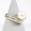 Ein 585/Gelbgold-Ring mit einer runden Zuchtperle und verziert mit brillanten Diamanten, präsentiert auf einem grauen, kegelförmigen Ständer.