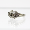 Ein 585/Weißgold-Ring mit zwei markanten runden Diamanten von insgesamt ca. 0,80 ct P1-2/H, begleitet von kleineren Diamanten, die in einem geometrischen Muster angeordnet und auf einer reflektierenden weißen Oberfläche präsentiert werden.