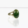 Der 333/Gelbgoldring mit Farbstein zeigt einen markanten, polierten grünen Edelstein, der in eine glatte, abgerundete Fassung eingefasst ist. Der Ring ruht auf einer reflektierenden weißen Oberfläche, die sein elegantes Design und seinen Glanz betont.