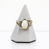 Der 333/Gelbgold Ring mit Opal und Zirkonia, mit einem ovalen weißen Opal in der Mitte und vier kleinen runden Zirkoniasteinen auf jeder Seite, wird auf einem grauen dreieckigen Ständer präsentiert.