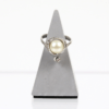 Ein 585er Weißgoldring mit einer markanten Perle in der Mitte, umgeben von sieben kleinen Diamanten mit insgesamt etwa 0,195 Karat, wird elegant auf einem dreieckigen grauen Ständer vor weißem Hintergrund präsentiert.