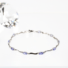 Das 585/Weißgold-Armband mit Farbsteinen zeigt eine Reihe kleiner violetter Edelsteine, die abwechselnd mit gebogenen Goldgliedern besetzt sind, auf einer weißen Oberfläche. Im Hintergrund ist ein facettierter klarer Kristall angebracht.