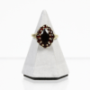 Der 585/Gelbgold-Ring mit Granat, der einen dunklen Edelstein im Marquiseschliff aufweist, der von kleineren runden Steinen umgeben ist, wird elegant auf einem hellgrauen, pyramidenförmigen Ständer vor einem schlichten weißen Hintergrund präsentiert.