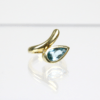 Der 585/Gelbgold Ring mit Aquamarin besticht durch ein abstraktes Design mit einem birnenförmigen blauen Edelstein. Er ruht auf einer reflektierenden Oberfläche, wodurch seine geschwungene Form und der Facettenschliff des Edelsteins betont werden.
