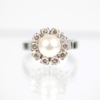 Ein Ring aus 585er Weißgold mit einer zentralen Perle, die von zehn Diamanten im Brillantschliff mit einem Gesamtkaratgewicht von ungefähr 1 Karat umgeben ist, auf einem reflektierenden Band angebracht.