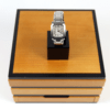 Die DAU Glashütte Original Lady Karrée (Referenznummer: 1201010104), eine Damenarmbanduhr aus Edelstahl mit rechteckigem Zifferblatt und römischen Ziffern, wird auf einem kleinen schwarzen Ständer präsentiert. Dieses Setup steht auf einer größeren Holzbox mit schwarzem Rand. Die Uhr verfügt außerdem über ein Metallgliederband und eine Faltschließe.