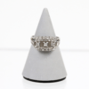 Ein 750/Weißgold-Ring, verziert mit drei Brillanten von insgesamt ca. 0,06 ct und zwölf kleinen Diamanten, präsentiert auf einem grauen, kegelförmigen Ständer vor weißem Hintergrund.