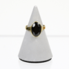 Ein Goldring mit einem ovalen Granat-Edelstein, genannt „750/Gelbgold Ring mit Granat“, wird elegant auf einem grauen, kegelförmigen Ständer vor einem schlichten weißen Hintergrund präsentiert.