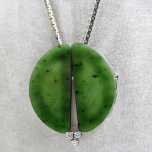 Eine 585/Weißgold-Kette mit Anhänger/Brosche, besetzt mit zwei halbrunden, an Jade erinnernden grünen Steinen und geschmückt mit einem Trio brillanter Diamanten von insgesamt etwa 0,15 Karat, hebt sich elegant vor einem hellgrauen Stoffhintergrund ab.