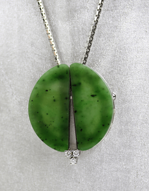 Eine 585/Weißgold-Kette mit Anhänger/Brosche, besetzt mit zwei halbrunden, an Jade erinnernden grünen Steinen und geschmückt mit einem Trio brillanter Diamanten von insgesamt etwa 0,15 Karat, hebt sich elegant vor einem hellgrauen Stoffhintergrund ab.