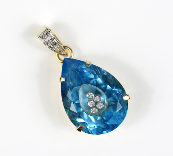 Ein Anhänger mit einem tropfenförmigen blauen Edelstein mit einer kleineren Träne im Inneren, verziert mit fünf kleinen Diamanten von insgesamt 0,25 Karat. Er ist in einen 750er Goldrahmen mit strukturierter Öse eingefasst, der ebenfalls mit kleinen Diamanten besetzt ist.