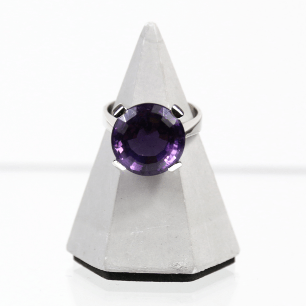 Ein 585er Weißgoldring mit einem Amethyst, präsentiert auf einem kleinen weißen Pyramidenständer vor einem schlichten weißen Hintergrund.