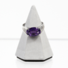 Ein 585er Weißgoldring mit einem Amethyst-Edelstein wird auf einem grauen pyramidenförmigen Ständer vor weißem Hintergrund präsentiert.